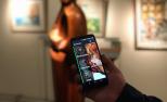 Una mano sujeta un teléfono con la aplicación Amuse frente a una escultura en un museo.