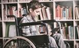 Un joven en silla de ruedas utiliza una tableta en una biblioteca.