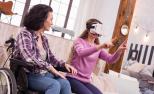Una mujer utiliza unas gafas de realidad virtual junto a otra mujer sentada en una silla de ruedas.