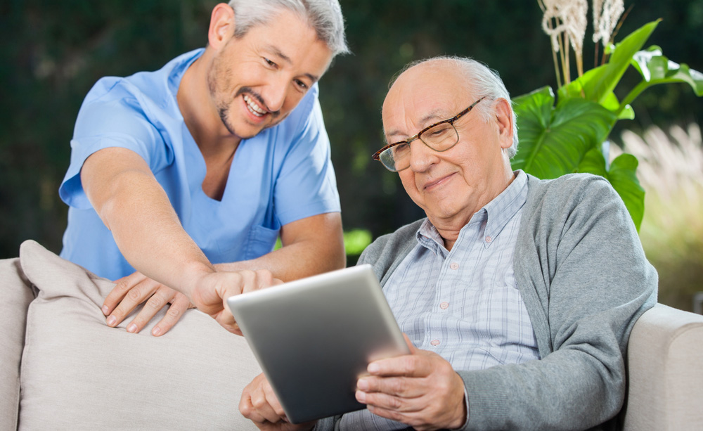 Una persona mayor utiliza una tableta junto a un asistente.